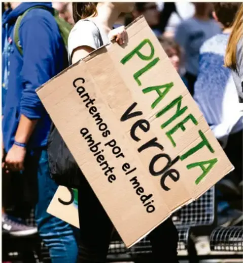 Persona sosteniendo un cartel de cartón con la frase 'PLANETA verde, Cantemos por el medio ambiente'.