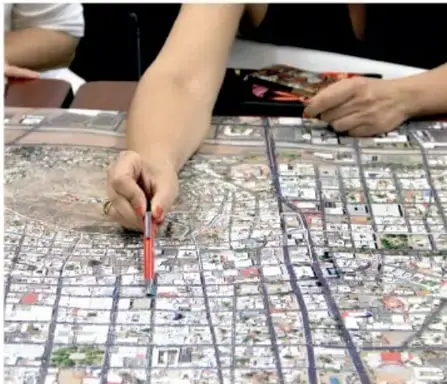 Manos de una persona señalando con un lápiz rojo sobre un mapa o croquis de una ciudad.