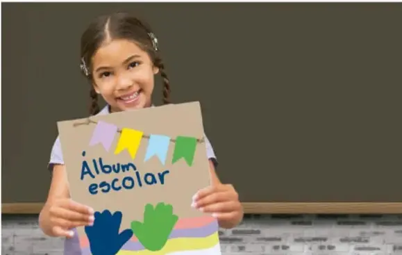 Niña sonriente sostiene una cartulina con el texto 'Álbum escolar' decorada con banderines y manos de colores.
