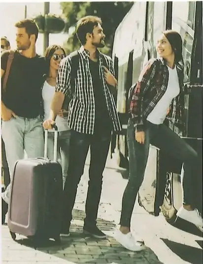 Fotografía de un grupo de jóvenes (hombre y dos mujeres) con maletas de viaje en una parada de transporte público, sonriendo. La imagen acompaña el texto 1 del ejercicio 1 sobre hermanos esperando el autobús. Crédito: Shutterstock (2020) 1217532163.