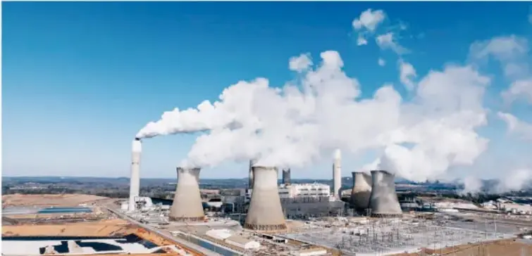 Fotografía de una central térmica o planta industrial con torres de refrigeración y chimeneas que emiten grandes nubes de vapor o humo blanco hacia el cielo, ilustrando la polución química.