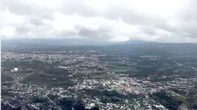 Fotografía aérea de un valle con una ciudad rodeada de montañas y nubes bajas, que ilustra el paisaje de la Sierra Norte de Puebla.