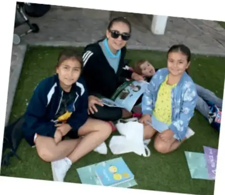 Fotografía de una madre y tres niñas sentadas en el pasto leyendo libros y revistas juntas.