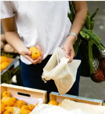 Fotografía de una persona sosteniendo una bolsa de tela con naranjas y verduras, que representa la compra de alimentos frescos y el uso de bolsas reutilizables.