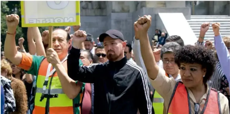 Grupo de personas con chalecos reflectantes y puños en alto durante una marcha o manifestación; representa la organización y solidaridad comunitaria.