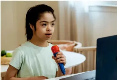 Niña con micrófono rojo hablando frente a una computadora, como si diera una noticia.