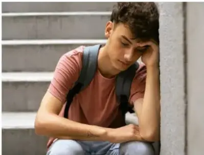 Fotografía de un adolescente sentado en escaleras, con la cabeza apoyada en la mano y expresión triste, representando el impacto emocional de la violencia.
