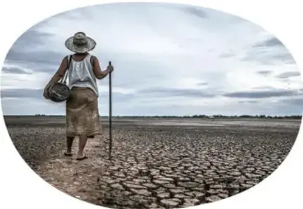 Mujer con sombrero caminando con bastón sobre terreno de tierra agrietada y seca, representando la escasez del agua.