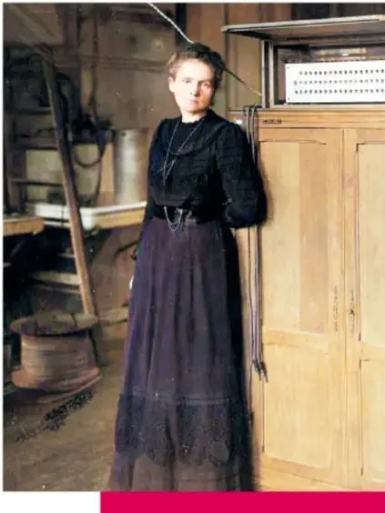 Fotografía antigua coloreada de Marie y Pierre Curie: él sentado con traje oscuro y barba, ella de pie con blusa blanca, posando juntos.