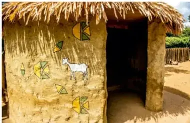 Foto de una choza de adobe con techo de paja, puerta de madera y paredes decoradas con pinturas de colores geométricos y animales.