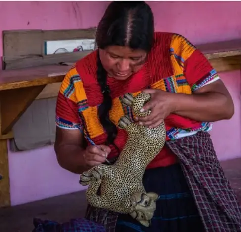 Mujer indígena maya (huipil de colores) trabajando artesanía con un objeto de pelaje de jaguar en un taller.
