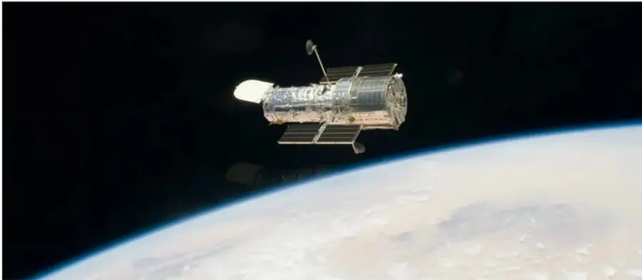 Fotografía de un telescopio espacial (tipo Hubble) en órbita, con la curvatura de la Tierra visible debajo de él.