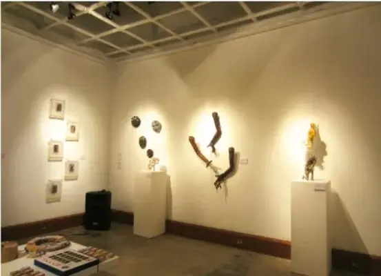 Fotografía de una sala de exposición con cuadros, esculturas y objetos sobre pedestales.