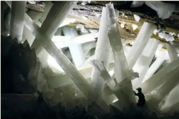 Fotografía de la Cueva de los Cristales de Naica con enormes vigas de selenita blanca y la silueta de una persona que muestra la escala gigantesca.