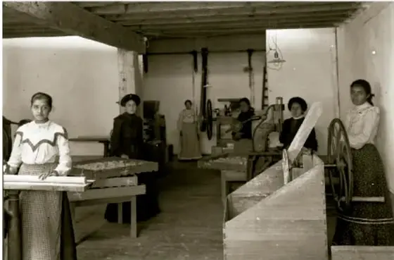 Fotografía en blanco y negro de una fábrica textil durante el Porfiriato. Se observan varias mujeres trabajando en máquinas de coser o telares, con vestimenta de la época.