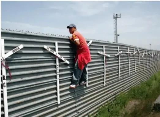 Fotografía de un trabajador con camisa roja y gorra subido a una estructura metálica de una obra en construcción, con casco y herramientas; al fondo se observa un cielo nublado y una torre de luz.