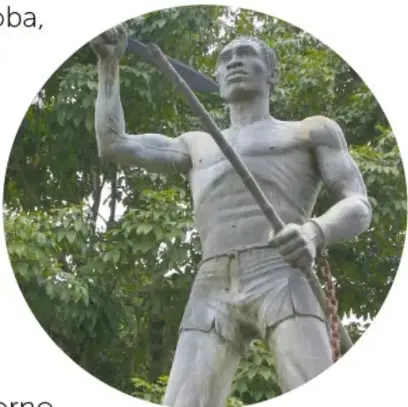 Fotografía circular de la estatua de Yanga: hombre fuerte con machete levantado y cadenas rotas en las muñecas, entre árboles.