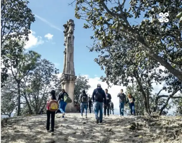 Grupo de personas con mochilas caminando por el cerro hacia un monumento de piedra entre árboles.