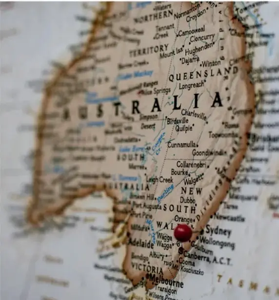 Fotografía de un mapa físico de Australia con un chinche rojo clavado sobre la región oriental; se aprecian nombres de ciudades como Sydney, Melbourne, Adelaide y Brisbane.