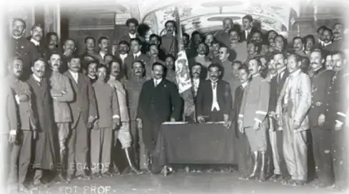 Fotografía histórica en blanco y negro que muestra a un grupo numeroso de hombres, muchos con traje y sombrero, reunidos frente a un edificio; parece corresponder a los participantes de la Convención de Aguascalientes.