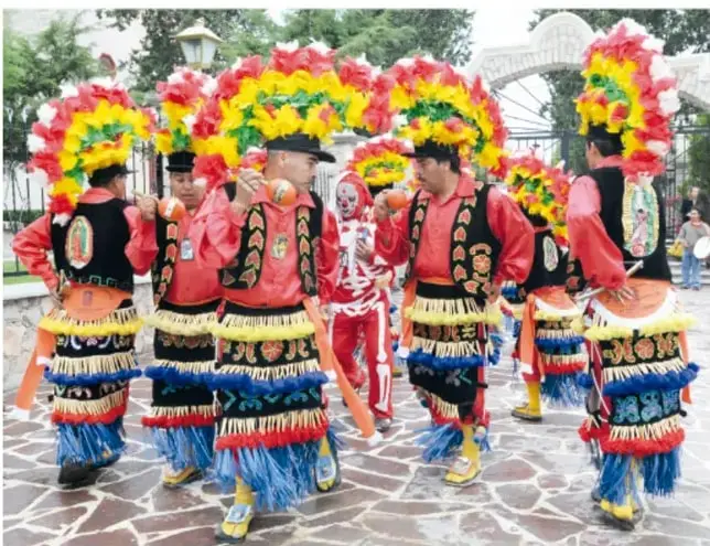 Fotografía de participantes del baile de los comanches en Veracruz, vestidos con trajes coloridos con penachos de plumas, acompañados de un personaje disfrazado de catrina (esqueleto).