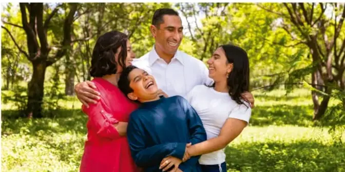 Fotografía de una familia (padres e hijos) abrazándose en un parque, transmitiendo protección y afecto.