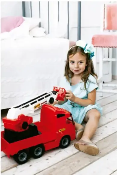 Niña sentada en el suelo de una habitación jugando con un camión de bomberos rojo.