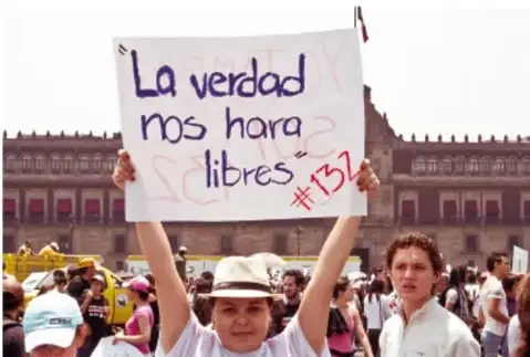 Persona sostiene un cartel que dice 'La verdad nos hará libres #131' frente a un edificio público.