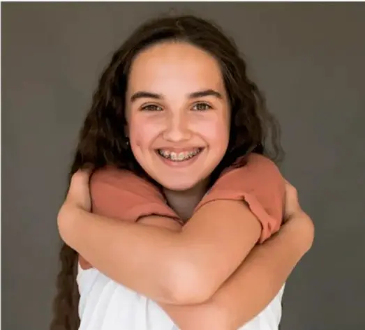 Fotografía de una joven sonriente que se abraza a sí misma, transmitiendo autoaceptación y bienestar.