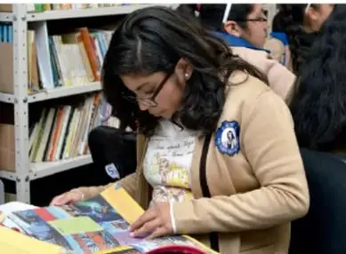 Fotografía de estudiantes en una biblioteca revisando libros y materiales impresos.