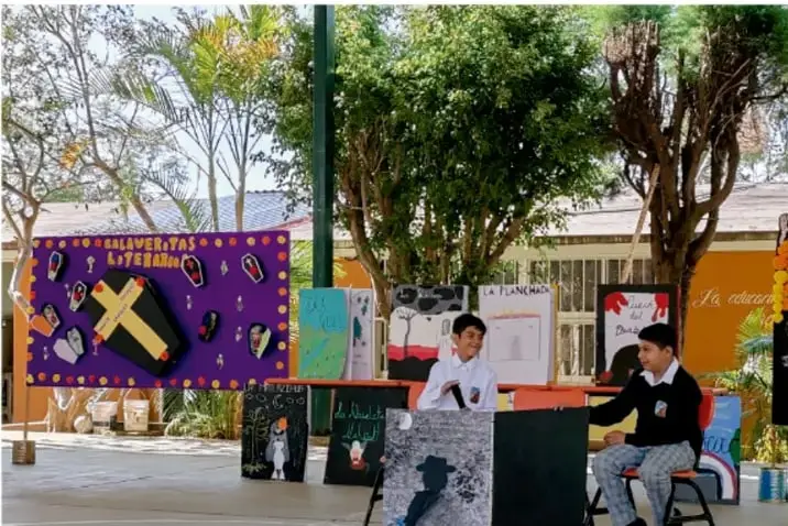 Fotografía de estudiantes en un patio escolar presentando su exhibición de arte con murales y pinturas en madera.