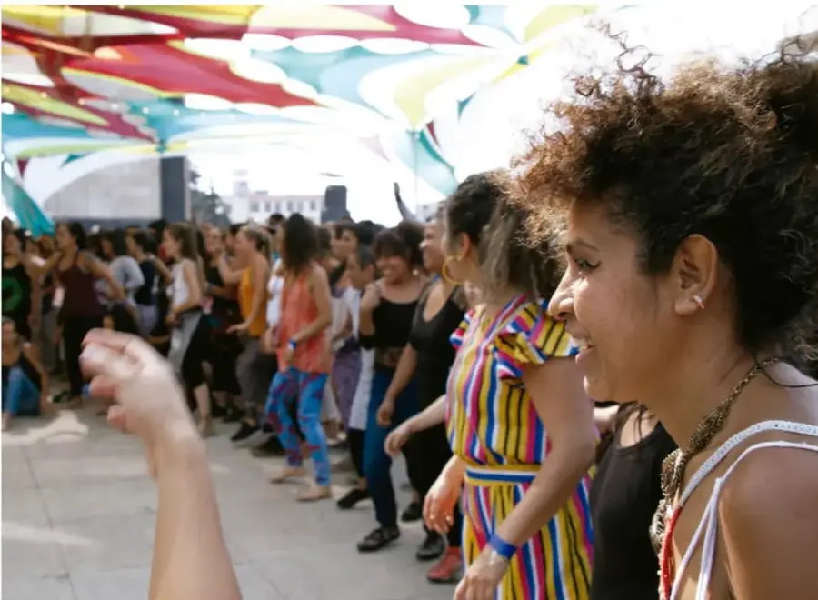 Fotografía de un grupo de personas practicando una actividad física o de danza al aire libre bajo toldos de colores, en actitud alegre y colaborativa.