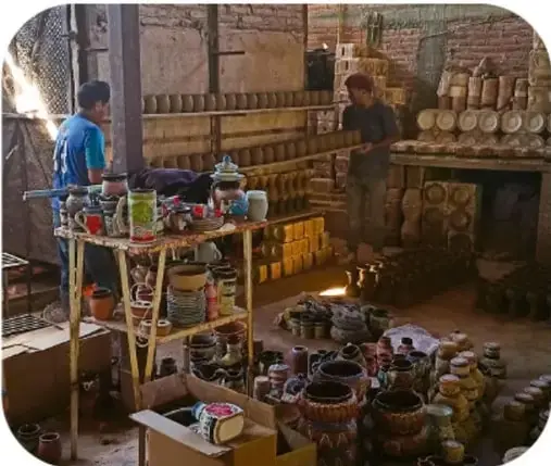 Fotografía de un taller de cerámica con gran cantidad de jarros, platos y vasos de colores apilados en el suelo.