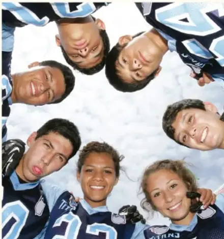 Fotografía de un grupo de adolescentes con uniforme deportivo azul y blanco, tomada desde abajo, sonriendo y formando un círculo con las cabezas al centro.