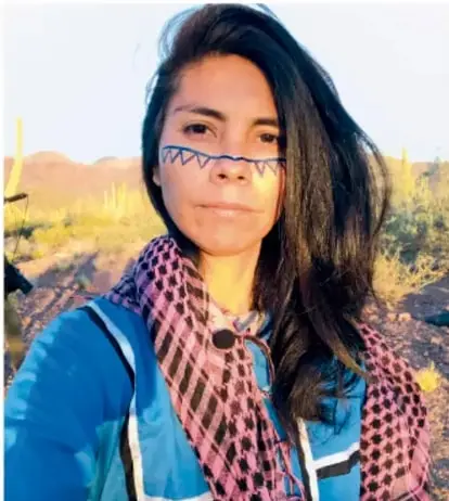 Fotografía de una joven indígena con pintura facial y un rebozo de colores, en un entorno de desierto con cactus, representando a los hablantes de las lenguas originarias.