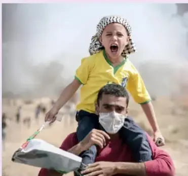 Fotografía de un hombre que carga en hombros a un niño que grita; el niño lleva un pañuelo en la cabeza y el hombre un cubrebocas; aluden a los conflictos territoriales y la guerra en el mundo.