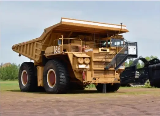 Camión minero amarillo de gran tonelaje (marca Caterpillar, número 166) estacionado sobre terreno de tierra.