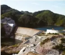 Presa de concreto con embalse de agua entre montañas boscosas.