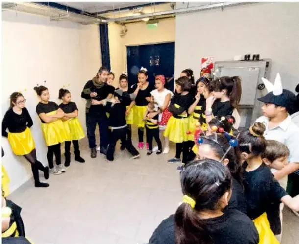 Fotografía de un grupo de estudiantes de primaria ensayando una obra de teatro en un salón, con vestuario y utilería.