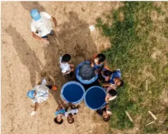 Vista aérea de personas con recipientes azules en terreno con vegetación