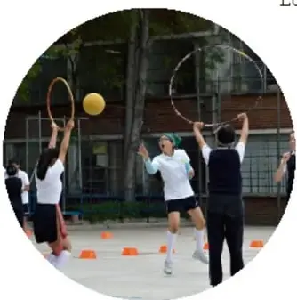 Estudiantes en un patio escolar practicando con aros y un balón junto a un profesor; ejemplo de tareas motrices.