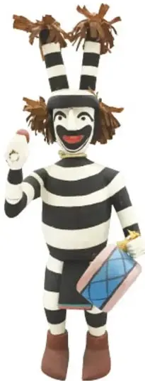 Figura de personaje ceremonial a rayas blancas y negras, con penacho de paja, boca sonriente pintada y tambor azul pequeño en la mano.