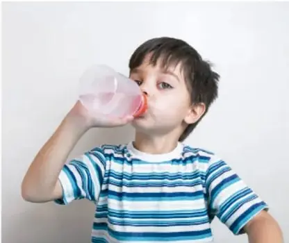 Niño con playera de rayas bebiendo agua de una botella en un bebedero.