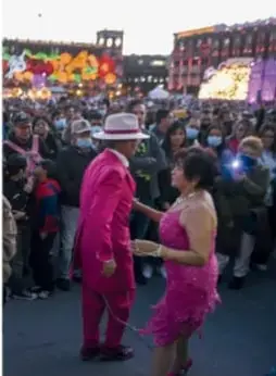 Personas bailando en una calle con vestimenta típica y globos, en un ambiente festivo.
