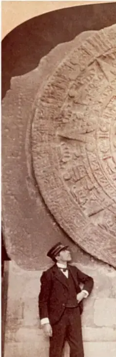 Fotografía en blanco y negro de un hombre con traje y sombrero observando la Piedra del Sol o Calendario Azteca, tallada en piedra.