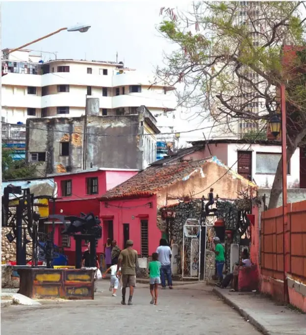 Fotografía de una calle urbana con viviendas de distintos niveles socioeconómicos: edificios modernos al fondo y casas modestas de colores en primer plano, con personas caminando. Ilustra la convivencia de estratos y la desigualdad en el entorno urbano.