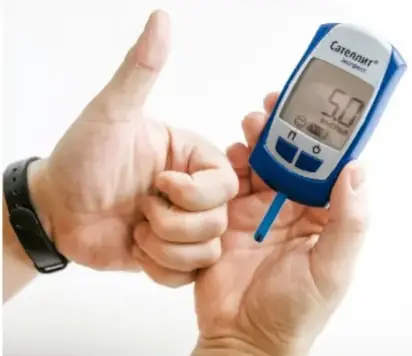 Fotografía de manos sosteniendo un glucómetro que muestra un nivel de glucosa de 5.0, usado para controlar la diabetes.