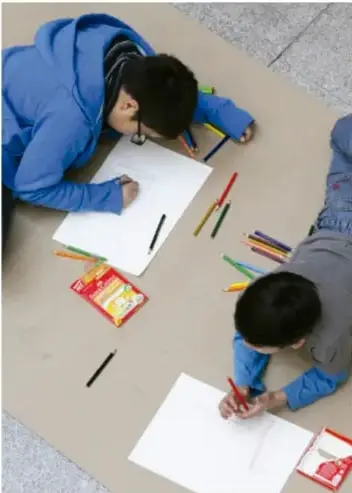 Fotografía de dos niños dibujando sobre papel en el suelo.