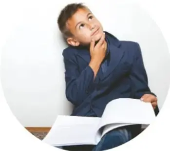 Niño con uniforme escolar pensando, con un libro abierto sobre sus piernas.