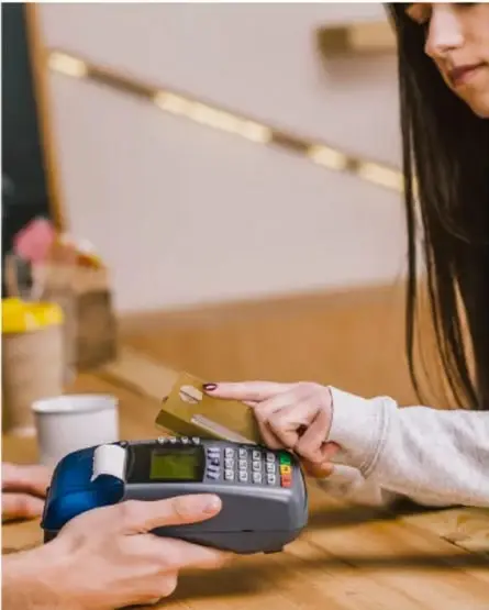 Fotografía de una persona realizando un pago con tarjeta en una terminal de punto de venta (datáfono), ilustrando la transacción comercial y el precio de venta de un producto o servicio.